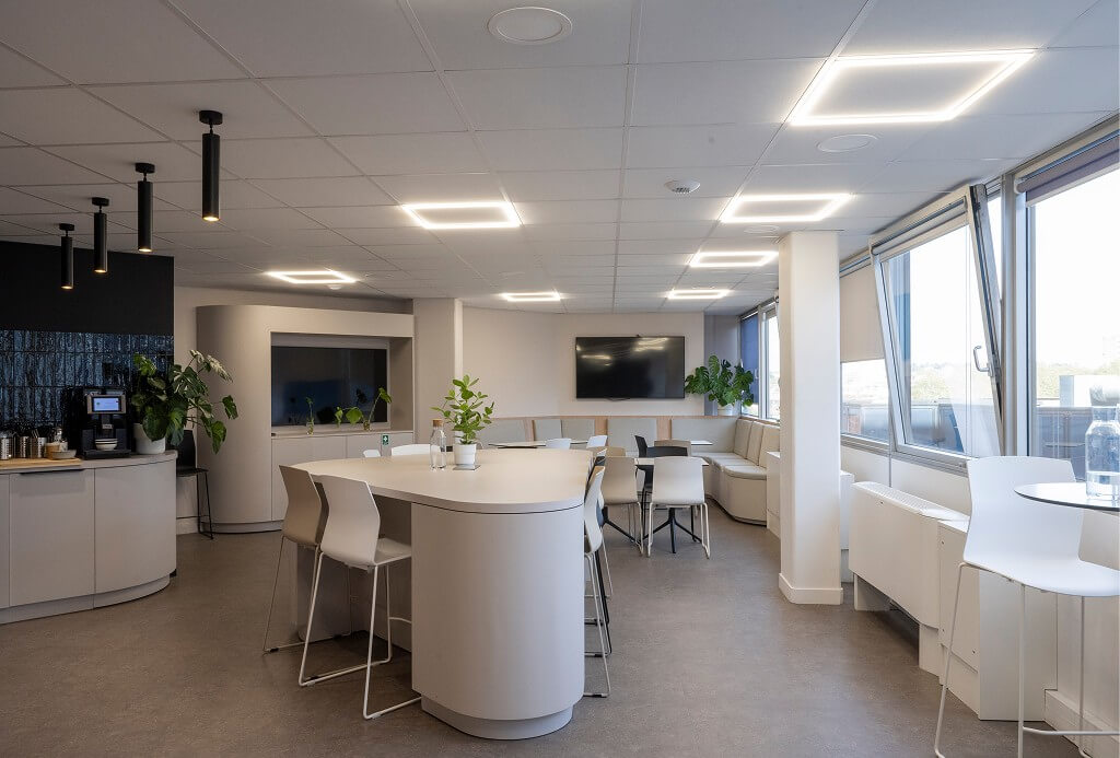 Espace détente lumineux dans une entreprise, avec mobilier arrondi design, grandes baies vitrées, plantes vertes et coin café équipé – ambiance conviviale et épurée.